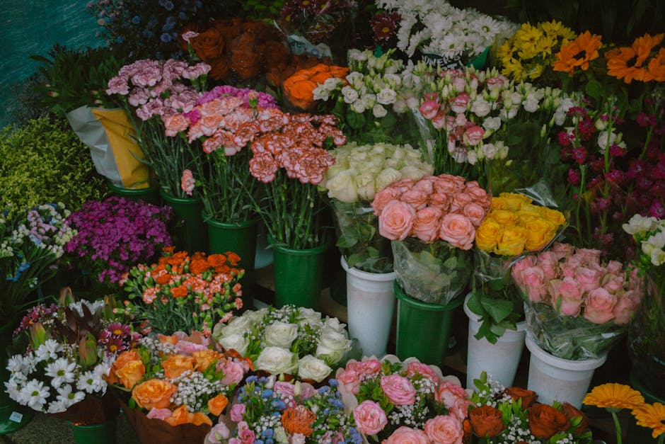 A vibrant display of fresh floral arrangements at a flower shop, featuring a variety of roses, carnations, daisies, and other colorful blooms in shades of pink, yellow, orange, white, and purple. The 